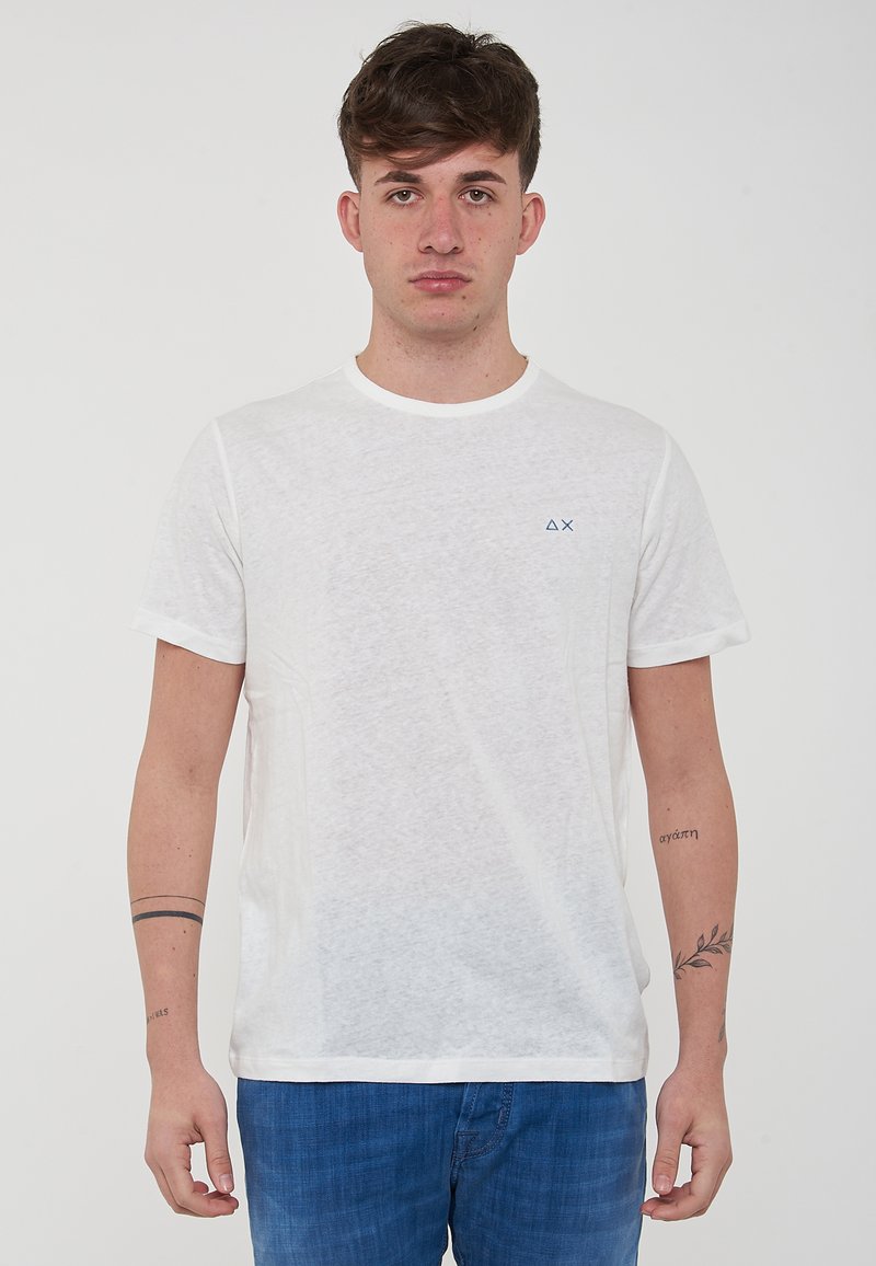 T-shirt bianco a maniche corte con collo rotondo, realizzato in tessuto leggero, con un piccolo logo blu sulla parte sinistra del petto.