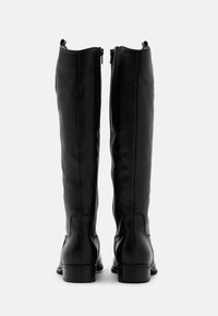 Bottes en cuir noir montantes, avec une texture lisse, fermeture zippée sur le côté et un petit talon droit. Les coutures apportent de la structure.