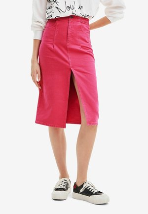 Roze denimrok tot de knie met een voorknip, hoge taille en riemlussen, gecombineerd met zwart-witte sneakers met een gestructureerde zool.