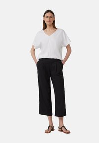 Witte, kortom mouwloze top met V-hals, gecombineerd met zwarte, wijde, geplooide broek. Sandalen hebben een zwarte band met een gouden accent.