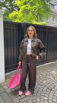 Bruine leren bomberjack, witte crop top, donkerbruine wijde broek, roze geblokte tote bag en roze schoenen met plateausole.