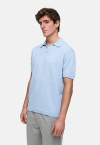Lys blå kortermet polo skjorte med teksturert stoff, krage og subtilt mønster. Kombinert med lysegrå bukser.