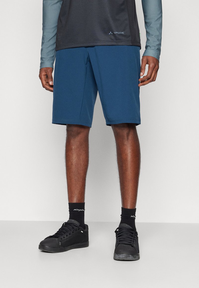 Blue shorts made of lightweight fabric, featuring a relaxed fit and a subtle logo detail near the hem, paired with black sneakers and socks.
