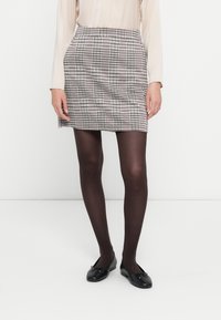 Ternede mini skirt i sort og hvid, med en glat stofstruktur og en tætsiddende talje. Sorte balletflade sko er iført.