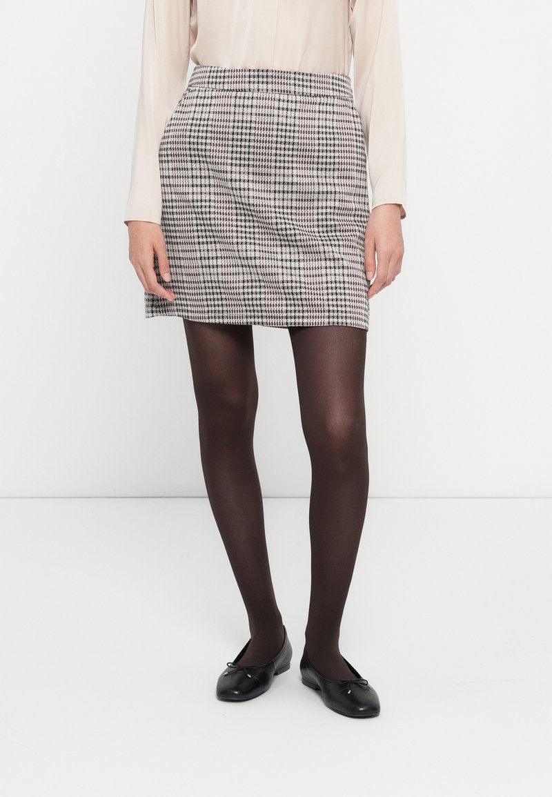 Ternede mini skirt i sort og hvid, med en glat stofstruktur og en tætsiddende talje. Sorte balletflade sko er iført.