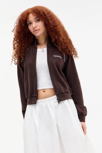 Pruun zip-up dressipluus valgete detailidega, soonilised mansetid ja hem, kantud valge lühikese tank topi peal. Pehme tekstuur, mugav lõige.