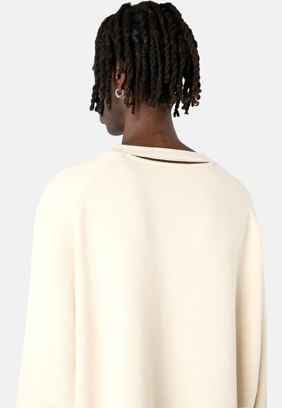 Cremefarbener Pullover mit lockerem Schnitt, mit einem Rückenausschnitt und gerippten Bündchen. Stricktextur, minimale Nähte und weicher Stoff.