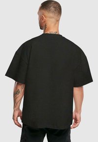Sort oversized t-shirt med korte ærmer, lavet af bomuldsstof, med rund halsudskæring og en ensfarvet tekstur, set fra ryggen.