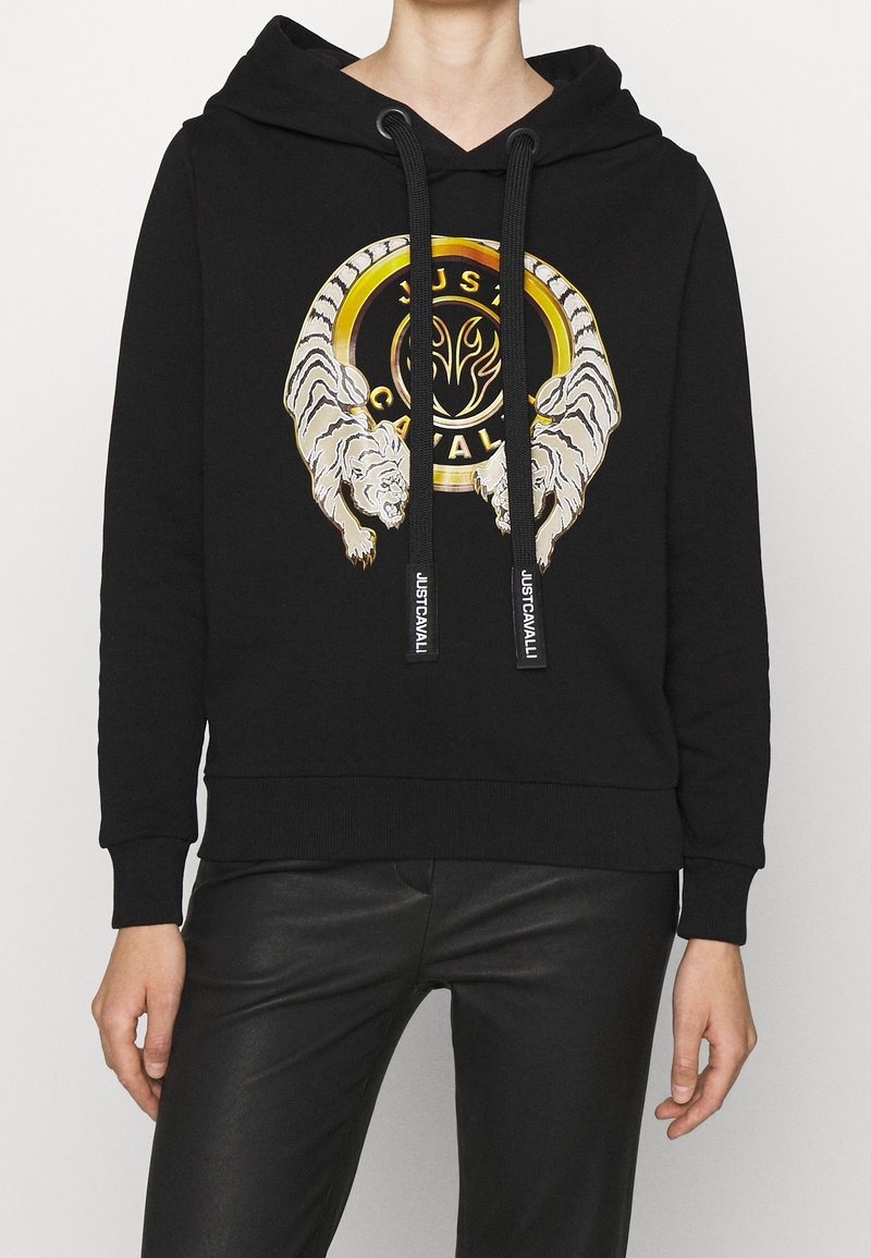 Haut à capuche noir avec un col en V, présentant un graphique de deux tigres et un logo circulaire avec des accents dorés. Fabriqué en tissu doux avec des poignets côtes.