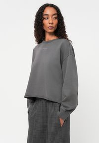 Grijze cropped sweatshirt van een katoenmix met een ronde halslijn en geribde manchetten. Gecombineerd met een grijze broek met een geruit patroon.
