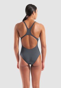 Harmaa urheilullinen yksiosainen uimapuku ristiin menevillä taustahihnoilla ja leikkausyksityiskohdilla, valmistettu sileästä ja joustavasta kankaasta.