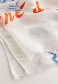 Leichter Schal aus weißem Stoff mit buntem Text und abstrakten Designs in Rot und Blau. Die Ränder sind leicht ausgefranst für eine texturreiche Optik.