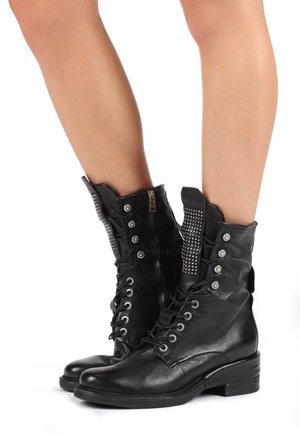 Botines de cuero negro con cordones, cremallera lateral, tachuelas plateadas en la parte superior y un tacón bajo de bloque. Textura lisa con acentos metálicos.