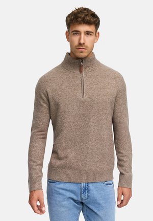 Brązowy sweter dzianinowy z wysokim kołnierzem i zapięciem na półsupeł. Żebrowane mankiety i dół, miękka tekstura, noszony z jasnoniebieskimi dżinsami.