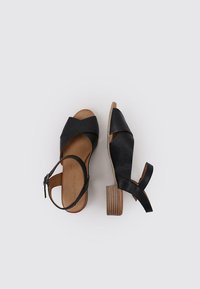 Sandalias de tacón negras de cuero que presentan un diseño de bandas cruzadas, tira en el tobillo y un tacón de bloque de madera. Textura suave y detalle de punta abierta.