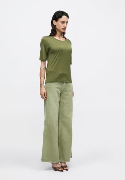 Top verde măsliniu cu mâneci scurte, combinat cu blugi largi, lejeri, de culoare verde deschis. Modelul poartă sandale maro cu toc înalt. Texturi simple și netede.