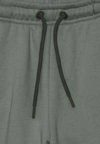 Pantaloni della tuta verde chiaro con un elastico in vita e un cordino nero, caratterizzati da una trama sottile. Senza modelli o dettagli visibili.