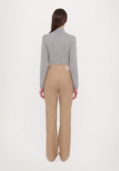 Grauer Rollkragenpullover mit langen Ärmeln, kombiniert mit hochtaillierten beigen Hose, die ein Markenetikett auf der Rückseite aufweist.
