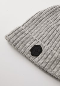 Gray knitted beanie with a ribbed texture and a black hexagonal patch featuring a logo on the folded cuff.