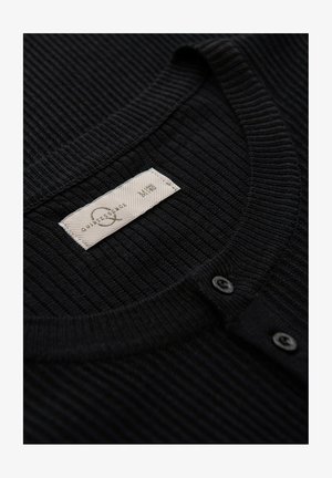 Schwarzer ribbeliger Pullover mit Rundhalsausschnitt, einer Frontblende mit zwei schwarzen Knöpfen und einem gewebten Etikett mit Pflegehinweisen.