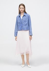 Μπλε ριγέ τζιν μπουφάν με δύο μπροστινές τσέπες, συνδυασμένο με φούστα από ροζ σατέν με δαντελωτό τελείωμα και λευκά παπούτσια με μυτερή μύτη.