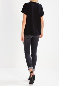 Top negro de manga corta con un ajuste holgado, combinado con unos jeans gris oscuro remangados en los puños y unos zapatos de tacón negros.