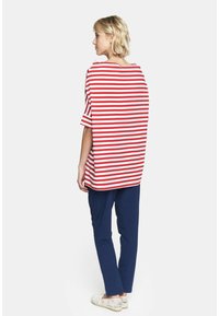 Czerwona i biała w paski, przesadnie duża koszula z krótkimi rękawami, zestawiona z granatowymi spodniami i beżowymi, koronkowymi butami wsuwanymi.