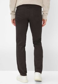 Donkerbruine slim-fit broek met twee achterzakken en subtiele textuur. Gekoppeld met witte sneakers, gezien van achteren.