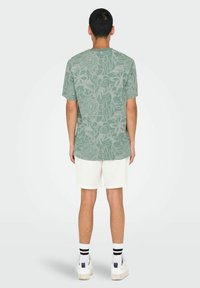 Camiseta verde de manga corta con patrón floral; hecha de una tela suave. Combinada con pantalones cortos blancos, calcetines a rayas blancos y negros, y zapatillas blancas.