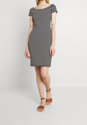 Robe ajustée à rayures noires et blanches avec des manches courtes et un col large. Portée avec des sandales brunes à lanières avec un talon compensé.