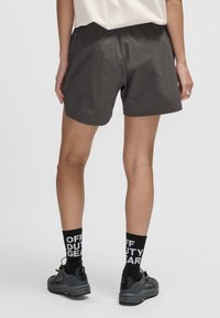 Grå idrottsshorts med resårmidja, slät textur och avslappnad passform, i kombination med svarta strumpor med vit text och grå skor.