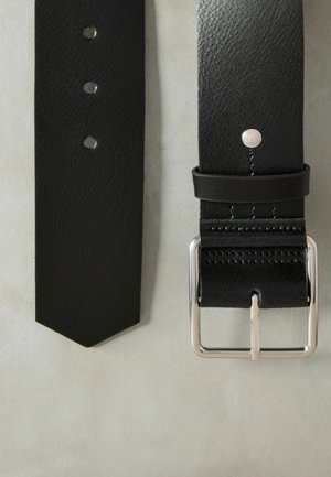 Čierny kožený opasok s textúrovaným povrchom, striebornou prackou a tromi dierkami na nastavenie. Výrazný špicatý koniec so subtilným akcentom blízko pracky.