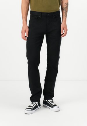 Jeans ajustados negros de denim, con un diseño clásico de cinco bolsillos y pasadores para cinturón. Llevados con zapatillas negras y blancas.