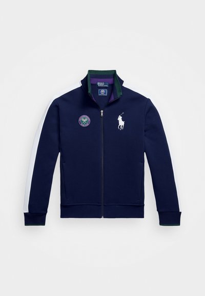 Chaqueta de tipo sudadera con cremallera en color marino, hecha de tela, que presenta franjas laterales blancas, un cuello verde, un logo bordado y puños y dobladillo acanalados.