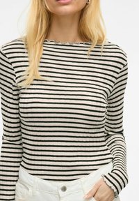 Zwart-wit gestreepte lange mouw top met een geribde textuur en een gegolfde halslijn, gecombineerd met witte hoge taille spijkerbroek.