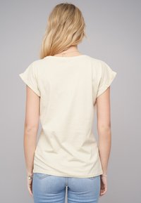 T-shirt jaune pâle à manches courtes avec des poignets retournés. Tissu léger, coupe ajustée et col rond. Texture lisse avec un minimum de détails.