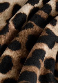 Měkká pletenina s leopardím potiskem v černé a hnědých tónech, zobrazená zblízka s viditelnou strukturou a záhyby.