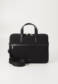 Sort taske med et håndtag på toppen, lavet af lærredsmateriale, med tekstureret overflade, sølvfarvede lynlåse, aftagelig skulderrem og et Calvin Klein-logo i bunden.