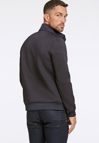 Mörkgrå sweatshirt med ståkrage, med en slät yta och ribbade muddar, i kombination med mörka jeans. Inga synliga logotyper eller mönster.