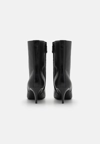 Botas de tornozelo em couro preto com altos saltos stiletto, apresentando um acabamento suave, silhueta angulada e fecho de correr na parte traseira.