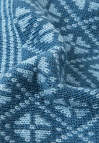 Dzianinowy koc w odcieniach niebieskiego, z geometrycznym wzorem i fakturowaną powierzchnią. Tkanina jest miękka, o tkanym wyglądzie.