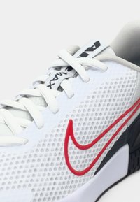 Nike-schoenen met een bovenwerk van wit mesh, een rode Swoosh-logo, grijze accenten en een zwarte buitenzool. Voorzien van traditionele vetersluiting en een gewatteerde kraag.