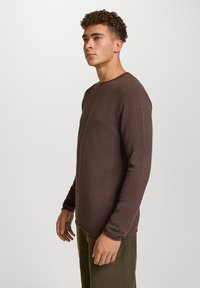 Brązowa koszula z długim rękawem o strukturalnym splocie, z okrągłym dekoltem i luźnym krojem, zestawiona z oliwkowymi spodniami.