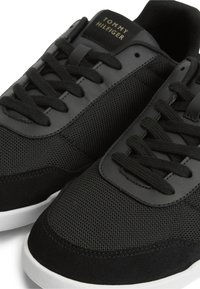 Μαύρα sneakers Tommy Hilfiger με πάνελ από δίχτυ και δέρμα, μαύρα κορδόνια και λευκές λαστιχένιες σόλες, σε κοντινή λήψη.