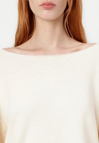 Light beige knit top with an off-shoulder neckline, featuring a soft texture and subtle ribbing. Edges show slight fraying details.