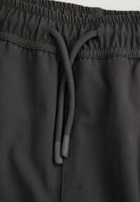 Czarne spodenki z elastycznym paskiem i wiązaniem na sznurek. Materiał ma gładką teksturę z subtelnymi pionowymi liniami.