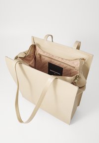 Beige lærveske med en strukturert design, som har en glidelåsinnredning og gullhardware. Innvendig stoff har et subtilt mønster.