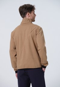 Chaqueta marrón de cremallera con alto cuello, fabricada en tejido texturizado y con acentos negros en los puños y el dobladillo, que presenta un logo en la parte posterior.