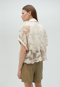 Lace top featuring floral patterns in cream with a relaxed fit and rolled sleeves, paired with olive green shorts.