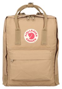 Beige Fjällräven Kånken ryggsäck med två handtag på toppen, framficka och en cirkulär logotyp med en röd räv. Tillverkad av slitstarkt material.